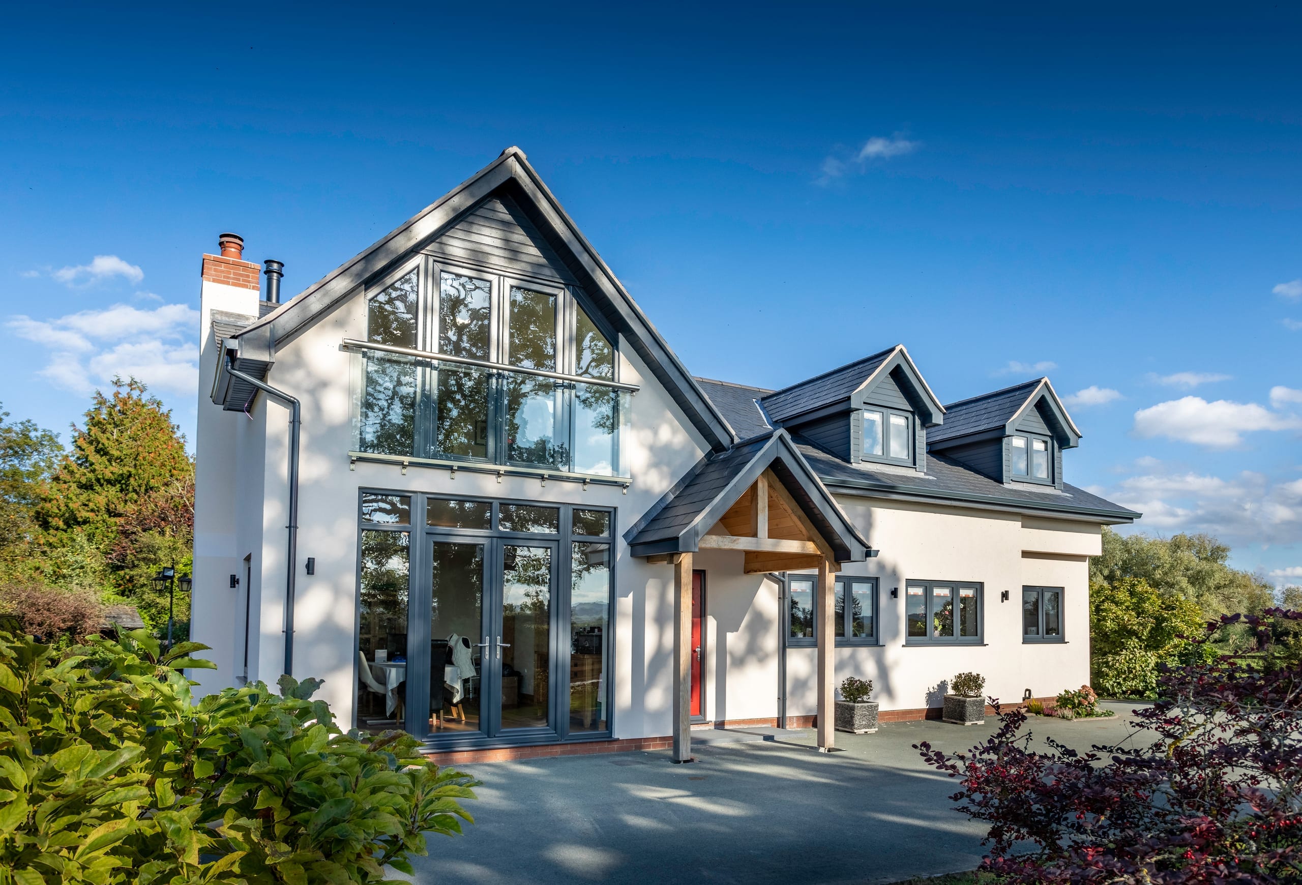 White rendered house with full-height gable glazing and grey aluminium windows
