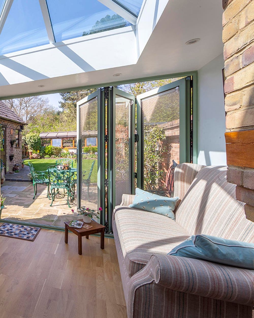 Sage-green bi-fold doors folded open from a garden room onto a patio