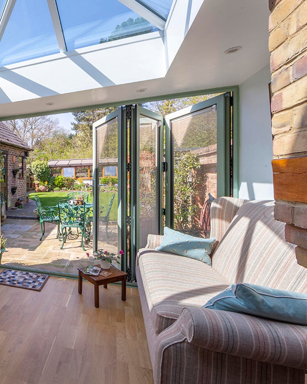 Sage-green bi-fold doors folded open from a garden room onto a patio