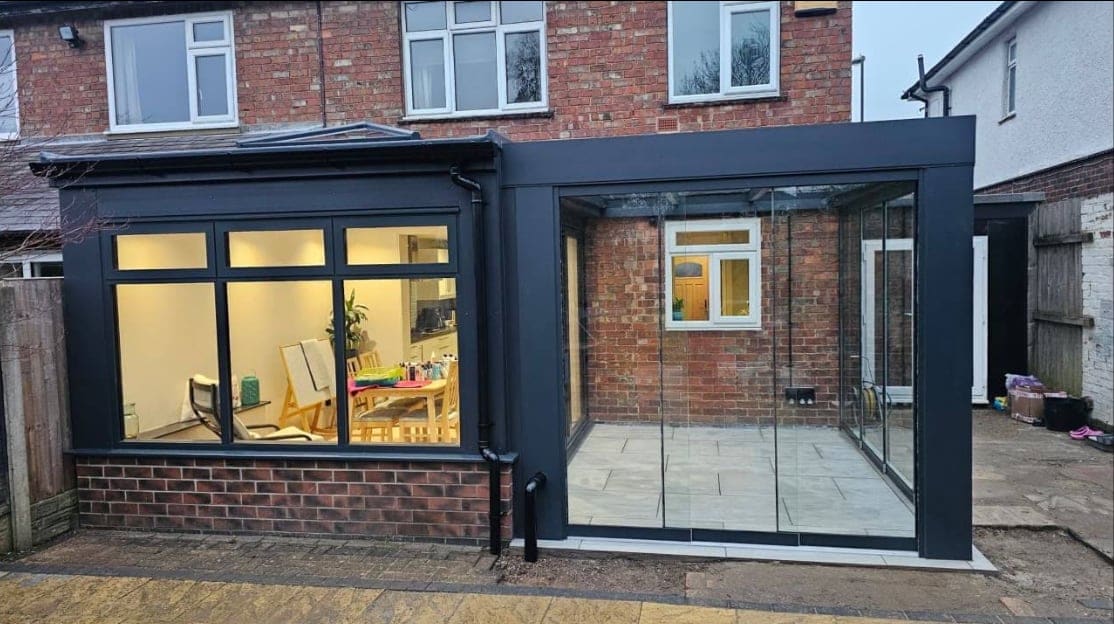 Anthracite glass extension with sliding doors on the back of a brick house